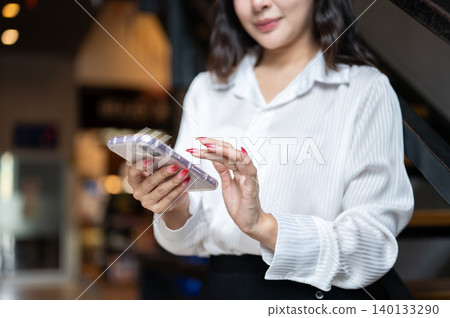 Close up of a woman's hands holding typing touching on smartphone while standing in dim cafe's room. Close up of a woman's hands holding typing touching on smartphone while standing in dim cafe's room. 140133290