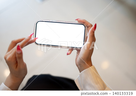 Close up of woman's long nails hands holding white screen phone as sitting indoors over tiles floor. Close up of woman's long nails hands holding white screen phone as sitting indoors over tiles floor. 140133319