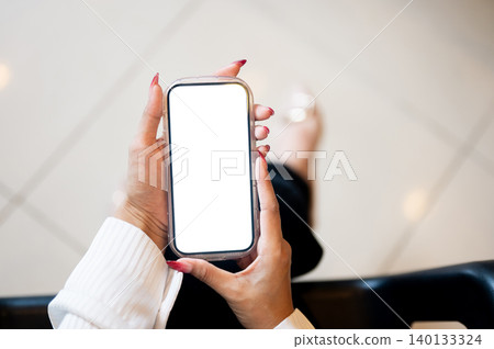 Close up of woman's long nail hands holding white screen phone while sitting indoors over tile floor Close up of woman's long nail hands holding white screen phone while sitting indoors over tile floor 140133324