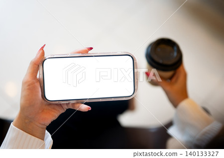 Close up of woman's long nails hand holding white screen phone in horizon and coffee sitting indoors Close up of woman's long nails hand holding white screen phone in horizon and coffee sitting indoors 140133327
