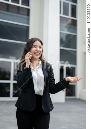 Pretty asian businesswoman talking on phone shrugging shoulder while standing outside the building. Pretty asian businesswoman talking on phone shrugging shoulder while standing outside the building. 140133360