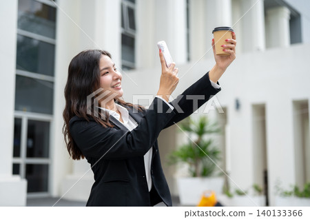 Pretty asian businesswoman holding phone taking photos of coffee cup while standing outside building Pretty asian businesswoman holding phone taking photos of coffee cup while standing outside building 140133366