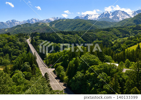 Tsugaike Panorama Park, enveloped in fresh greenery, and the snow-capped Hakuba mountain range in Otari Village, Nagano Prefecture (aerial photograph taken by drone). Tsugaike Panorama Park, enveloped in fresh greenery, and the snow-capped Hakuba mountain range in Otari Village, Nagano Prefecture (aerial photograph taken by drone). 140133399