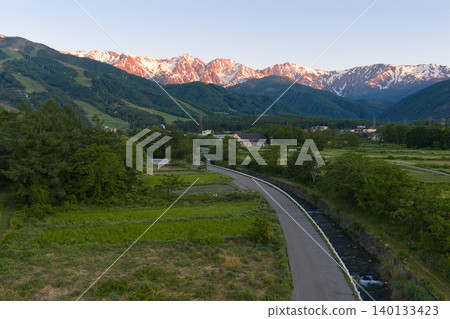The beautiful morning glow over the Hakuba Three Peaks and the lush greenery of Hakuba Village, Nagano Prefecture (aerial photography by drone) The beautiful morning glow over the Hakuba Three Peaks and the lush greenery of Hakuba Village, Nagano Prefecture (aerial photography by drone) 140133423