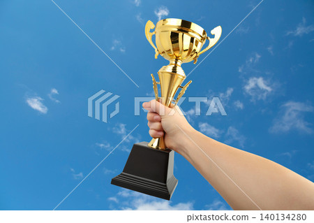 Hand holds a golden trophy up in the sky celebrating victory 140134280