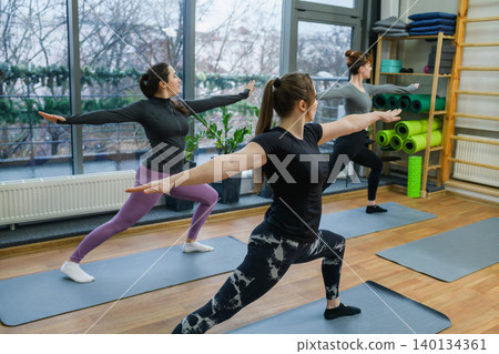 Three women practicing yoga warrior pose in studio Three women practicing yoga warrior pose in studio 140134361