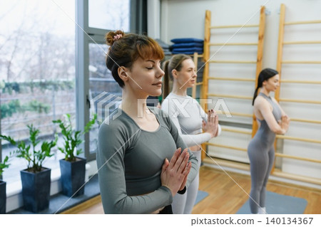 Women standing in prayer pose during yoga class 140134367