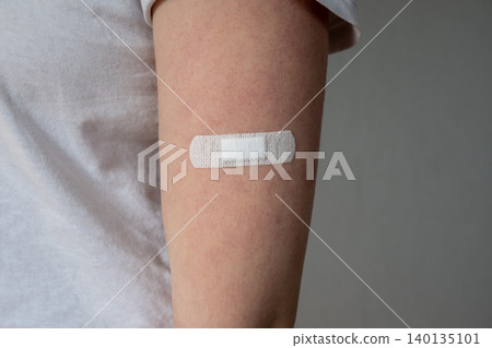 Young woman with medical adhesive plaster on the hand after vaccination. Fabric white bandage like first help for wound on the damage skin. Young woman with medical adhesive plaster on the hand after vaccination. Fabric white bandage like first help for wound on the damage skin. 140135101
