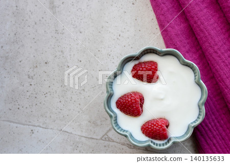 Fresh yogurt with raspberry berries in green porcelain plate on the stone table and cotton red napkin for healthy breakfast. Space fot text. 140135633