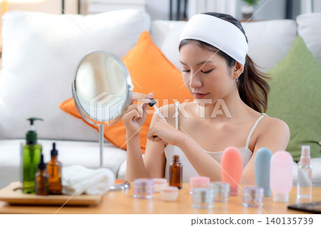 Beautiful young asian woman applying lotion herb on hands looking mirror at home. 140135739