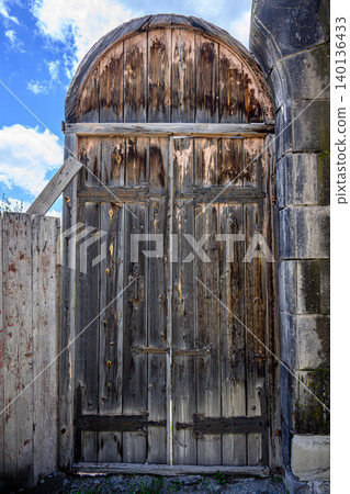 Weathered wooden gate with stone framing, under bright blue sky with clouds Weathered wooden gate with stone framing, under bright blue sky with clouds 140136433