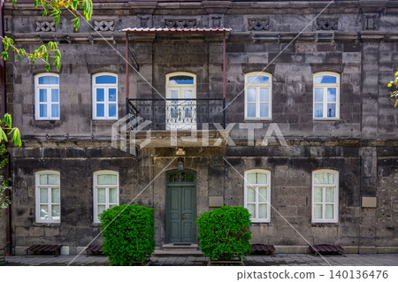 Old stone building with white-framed windows and green door. Decorative balcony with iron railing above entrance Old stone building with white-framed windows and green door. Decorative balcony with iron railing above entrance 140136476