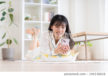 一位穿著睡衣的年輕女子正在看她的智慧型手機。 一位穿著睡衣的年輕女子正在看她的智慧型手機。 140136628