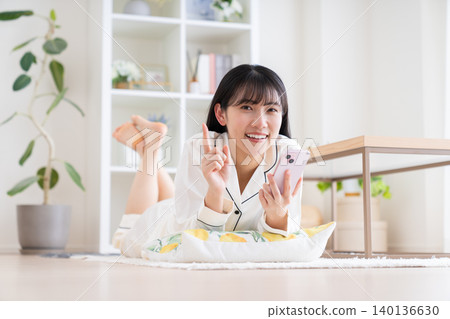 一位穿著睡衣的年輕女子正在看她的智慧型手機。 一位穿著睡衣的年輕女子正在看她的智慧型手機。 140136630