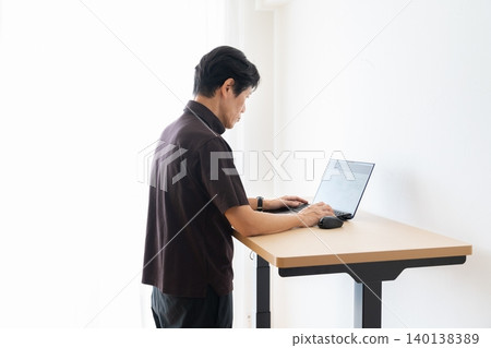 A middle-aged man using a computer at a standing desk. A middle-aged man using a computer at a standing desk. 140138389