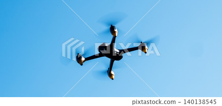 Black drone fllying in the blue sky. Innovative modern technology for work, game or entertainment. Black drone fllying in the blue sky. Innovative modern technology for work, game or entertainment. 140138545
