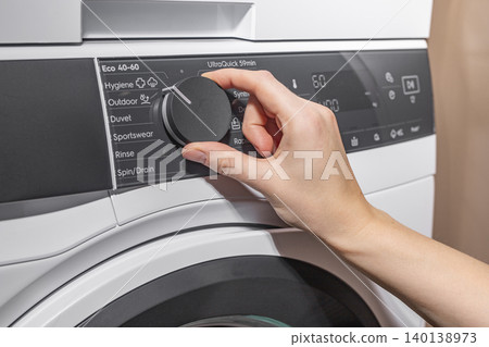 Woman turning washing machine program dial on control panel. Adult female adjusting front loading appliance settings in laundry room. Domestic cleaning concept for home, household, lifestyle Woman turning washing machine program dial on control panel. Adult female adjusting front loading appliance settings in laundry room. Domestic cleaning concept for home, household, lifestyle 140138973