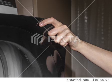Woman touching black drying machine door glass. Adult female hand in laundry room. Domestic washing concept for home, household, lifestyle.. Woman touching black drying machine door glass. Adult female hand in laundry room. Domestic washing concept for home, household, lifestyle.. 140138978