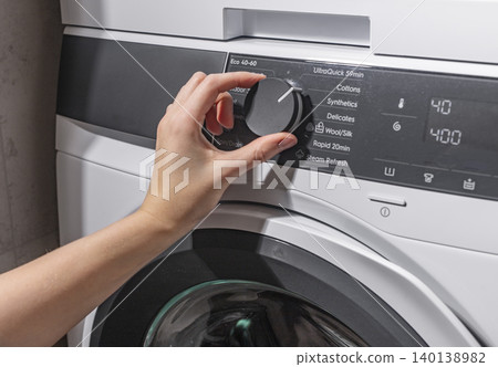 Woman rotating washing machine selector knob on control panel. Adult female setting program on front loading appliance. Domestic laundry concept for home, cleaning, household lifestyle.. Woman rotating washing machine selector knob on control panel. Adult female setting program on front loading appliance. Domestic laundry concept for home, cleaning, household lifestyle.. 140138982