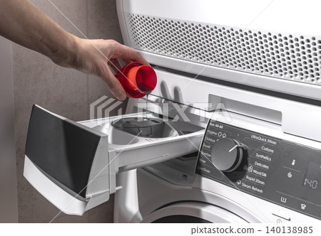 Woman pushing washing machine detergent drawer after adding liquid. Adult female closing appliance compartment in laundry room. Domestic washing concept for home, household, lifestyle.. Woman pushing washing machine detergent drawer after adding liquid. Adult female closing appliance compartment in laundry room. Domestic washing concept for home, household, lifestyle.. 140138985