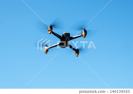 Black drone fllying in the blue sky. Innovative modern technology for work, game or entertainment. Black drone fllying in the blue sky. Innovative modern technology for work, game or entertainment. 140139583