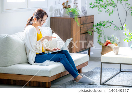 使用一台電腦在客廳裡的年輕女子 140140357