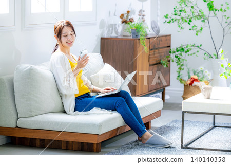使用一台電腦在客廳裡的年輕女子 140140358