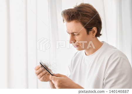 a worried man deals with male hair loss and alopecia. He looks at a comb full of fallen hair, a grooming stress related to testosterone a worried man deals with male hair loss and alopecia. He looks at a comb full of fallen hair, a grooming stress related to testosterone 140140887