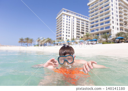Young boy snorkels in clear water at beachfront resort on sunny day 140141180