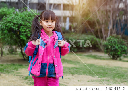 Happy Asian schoolgirl carrying a blue backpack walking home after school in the park Happy Asian schoolgirl carrying a blue backpack walking home after school in the park 140141242