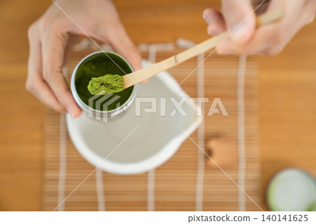Close up of woman hand scooping Matcha powder with bamboo spoon Close up of woman hand scooping Matcha powder with bamboo spoon 140141625