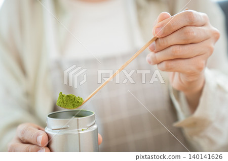 Close up of woman hand scooping Matcha powder with bamboo spoon Close up of woman hand scooping Matcha powder with bamboo spoon 140141626