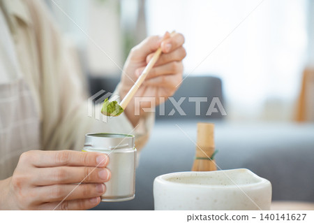 Close up of woman hand scooping Matcha powder with bamboo spoon Close up of woman hand scooping Matcha powder with bamboo spoon 140141627