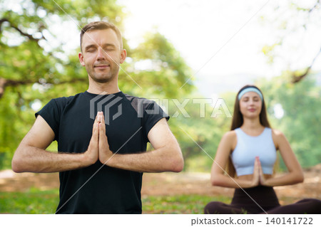 Peaceful man and woman practicing yoga meditation in a green park Peaceful man and woman practicing yoga meditation in a green park 140141722