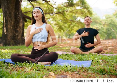 Young woman and man practicing breathing exercise in green park Young woman and man practicing breathing exercise in green park 140141730