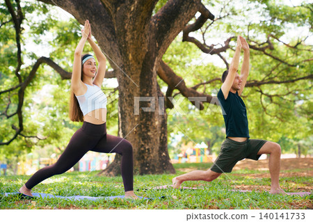 Young man and woman practicing warrior yoga pose in green park Young man and woman practicing warrior yoga pose in green park 140141733
