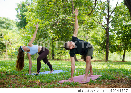 Morning wellness session with couple performing yoga in nature 140141737