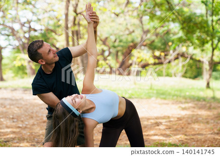 Yoga teacher adjusting posture for young woman at outdoor session 140141745
