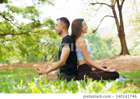 Peaceful man and woman practicing yoga meditation under large tree in park Peaceful man and woman practicing yoga meditation under large tree in park 140141746