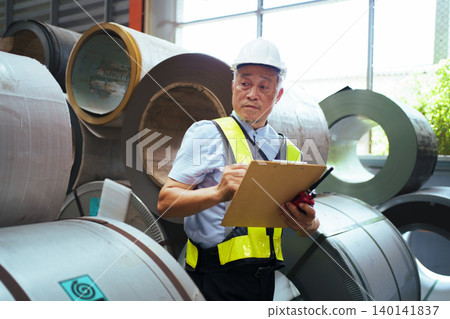 Senior factory foreman holding clipboard and walkie-talkie while checking factory. 140141837