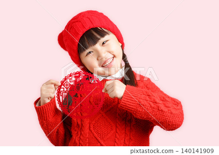 Happy Asian little girl holding Chinese paper cut decoration, wearing red sweater on pink background, festival celebration concept 140141909
