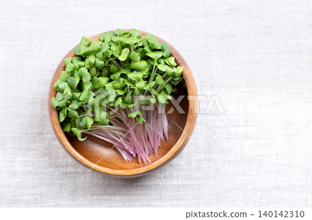 Red radish microgreens, fresh sprouts in a wooden bowl on linen. Young plants, seedlings, and cotyledons of Raphanus sativus, an edible root vegetable, mostly eaten raw. Close-up,  from above. Photo 140142310