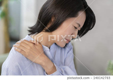 A profile view of a woman in her mid-40s holding her shoulder. A profile view of a woman in her mid-40s holding her shoulder. 140142783