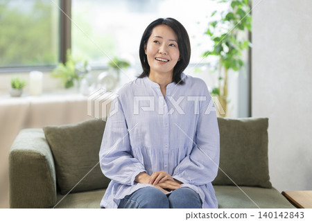 一位面帶微笑的中年婦女坐在沙發上。 一位面帶微笑的中年婦女坐在沙發上。 140142843