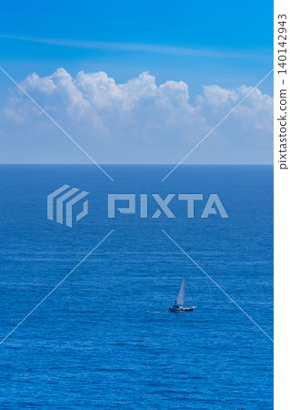 A small sailboat sailing beneath the blue summer sea and white clouds. A small sailboat sailing beneath the blue summer sea and white clouds. 140142943