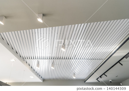 Ceiling with bright lights in a modern warehouse, shopping center building, office commercial real estate object. Directional LED lights on rails under the ceiling Ceiling with bright lights in a modern warehouse, shopping center building, office commercial real estate object. Directional LED lights on rails under the ceiling 140144309