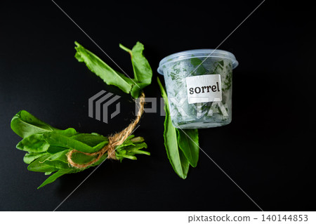 Green sorrel herb bunch with plastic container on black background 140144853