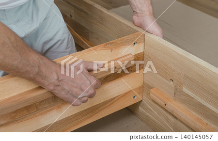 Wooden furniture assembly with hands fitting a timber joint. Close up of carpentry work in an indoor workshop. Home improvement and woodworking installation concept.. 140145057
