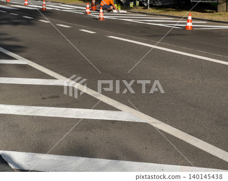 Brightly dressed workers are painting clear road markings on a busy street, ensuring safe navigation for vehicles and pedestrians alike Brightly dressed workers are painting clear road markings on a busy street, ensuring safe navigation for vehicles and pedestrians alike 140145438