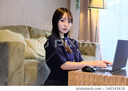 Working remotely from home. A woman working remotely in her living room, concentrating on her computer. Working remotely from home. A woman working remotely in her living room, concentrating on her computer. 140145618